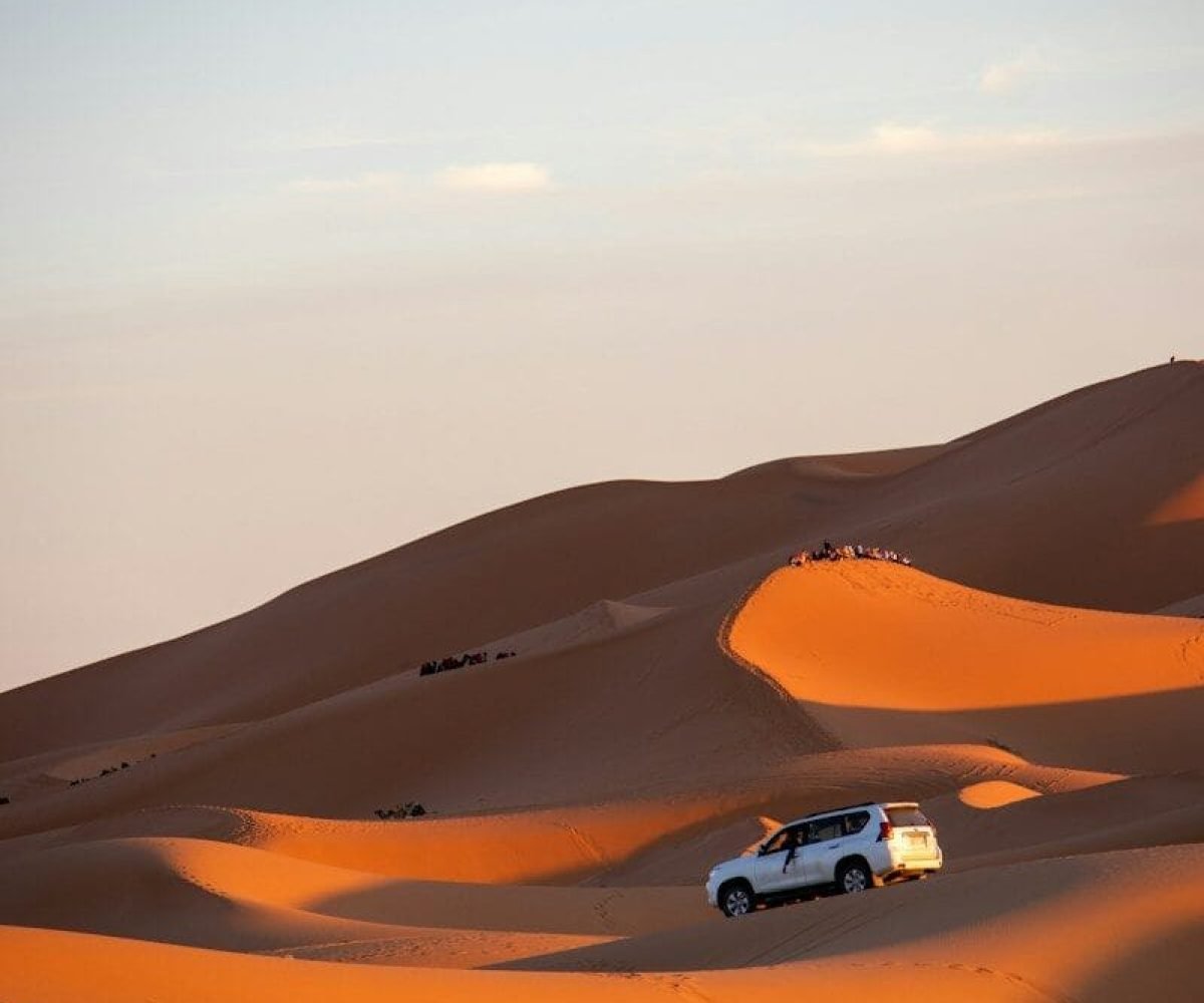 A car driving through the desert with sand dunes in the background