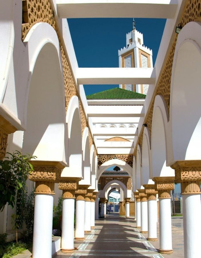 A walkway lined with columns and arches with a clock tower in the background