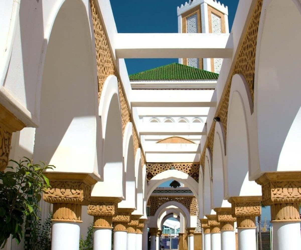 A walkway lined with columns and arches with a clock tower in the background