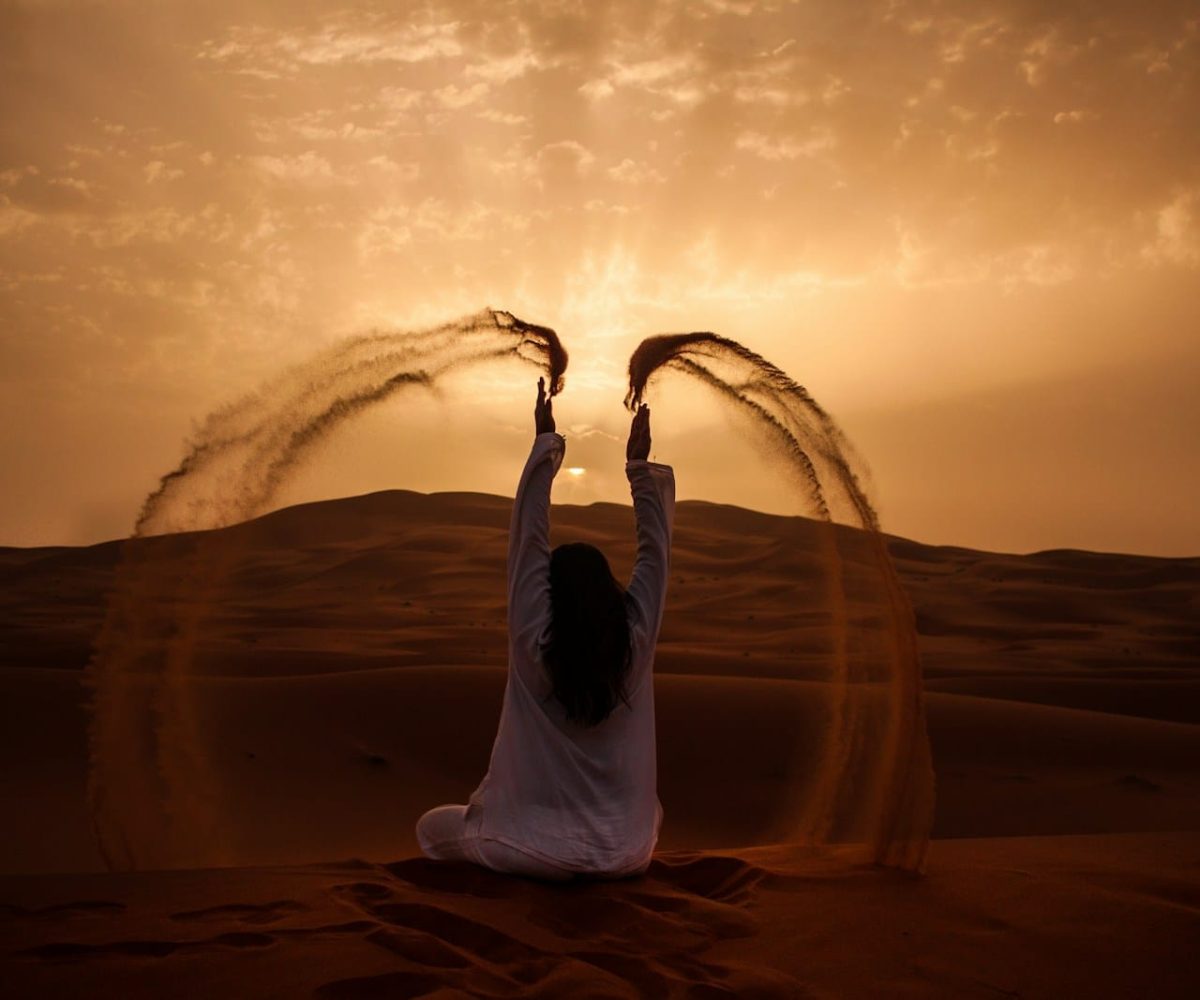 woman sitting on desert while playing sand during golden hour,marrakech to merzouga