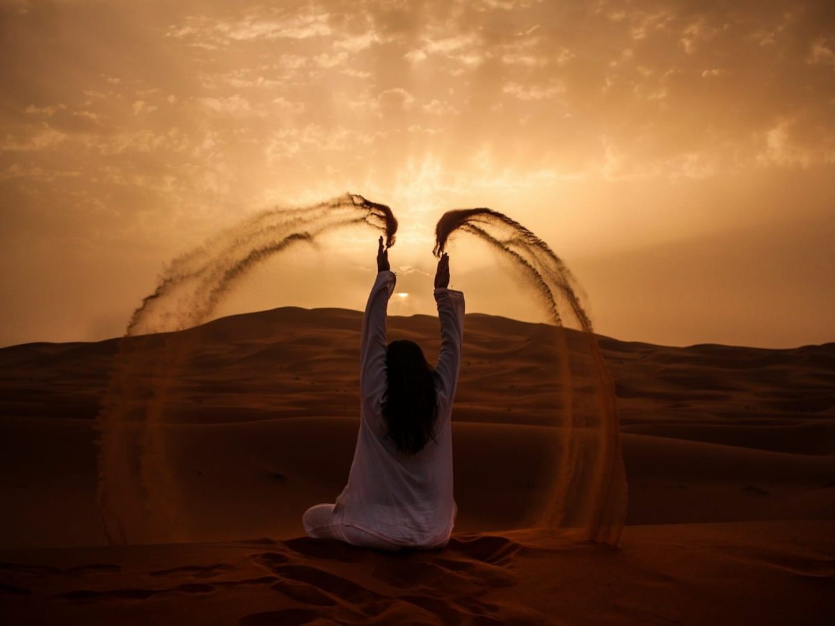 woman sitting on desert while playing sand during golden hour,3 days desert tour Marrakech to Fes