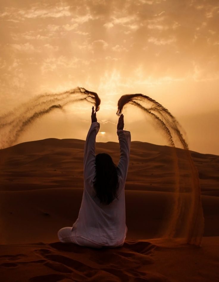 woman sitting on desert while playing sand during golden hour