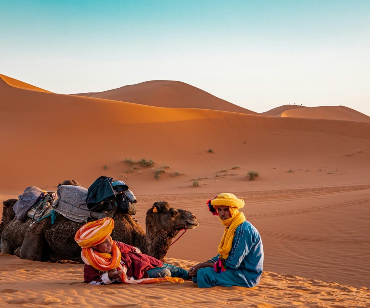 man in yellow robe sitting on brown sand during daytime,errachidia to merzouga
